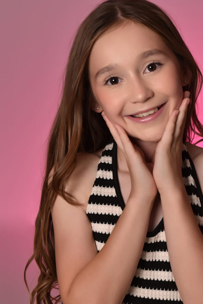 Smiling girl with her hands on her cheeks against a pink backdrop