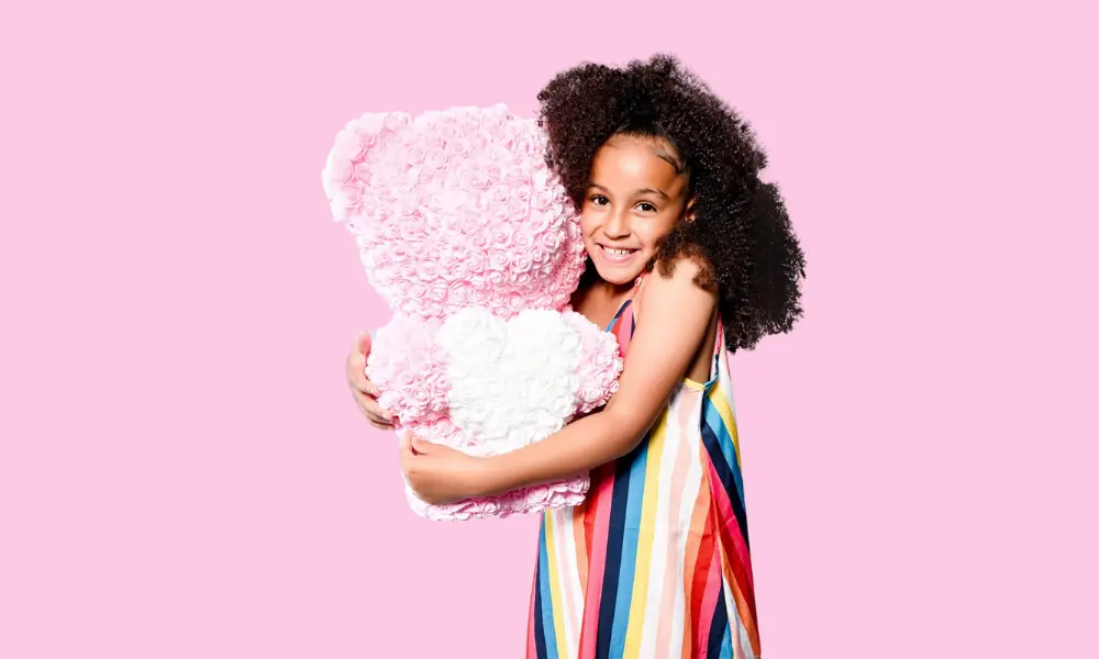 Smiling girl in a rainbow dress hugging a pink teddy bear
